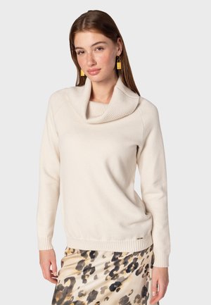 Beige sweater with a cowl neck, ribbed cuffs, and hem. Soft texture. Paired with a patterned skirt featuring shades of brown and cream.