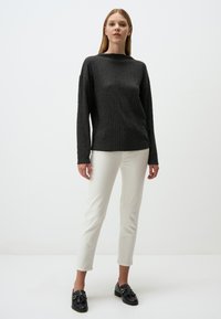 Un pull texturé gris avec des manches longues, un pantalon blanc slim-fit, et des mocassins noirs avec des accents dorés, sur un fond neutre.