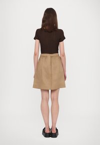 Brown textured short-sleeve top paired with a beige A-line skirt, featuring an elastic waistband and above-the-knee length. Black shoes.