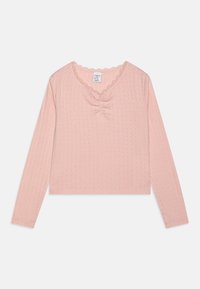 Light pink long-sleeve top with a V-neck, gathered center detail, and scalloped lace trim. Made from textured fabric with small patterns.