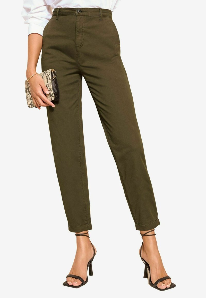 Pantalons vert olive à taille haute, jambe droite et ourlets roulés. Associés à des talons aiguilles noirs à brides et à une pochette à motifs serpent.