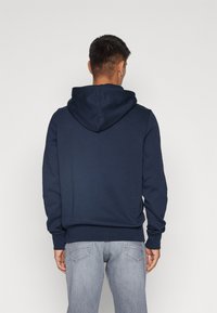 Sudadera de algodón azul marino con cordón y un gran bolsillo, con un corte holgado y puños acanalados, combinada con jeans gris claro.