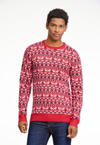 Röd mönstrad tröja med vita renar och gröna träd, med en ribbad halsringning och ärmslut. Materialet har en stickad struktur.