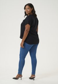 Un haut noir à manches courtes associé à un jean skinny bleu et des talons noirs. Le haut présente une coupe décontractée et un col rond.