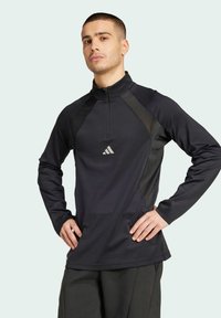 Zwarte atletische longsleeve shirt met een halve rits kraag, contrasterende zijpanelen en een klein reflecterend logo op de borst.