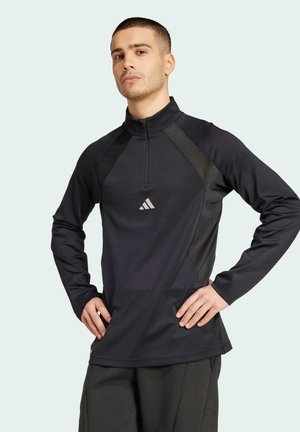 Schwarzes, athletisches Langarmshirt mit einem halben Reißverschlusskragen, kontrastierenden Seitenpanelen und einem kleinen reflektierenden Logo auf der Brust.