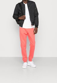 Svart bomberjacka, vit t-shirt och korallfärgade sweatpants. Modell bär vita sneakers. Jackan har dragkedjor och en standardpassform.