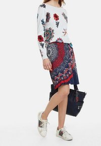 Blommönstrad vit tröja, marinblå mönstrad kjol och vita sneakers med färgglada detaljer. Svart handväska. Avslappnad outfit.