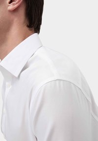 Witte button-up overhemd met een gestructureerde kraag, een gladde textuur en een aansluitende snit, met een minimalistisch ontwerp en strakke lijnen.