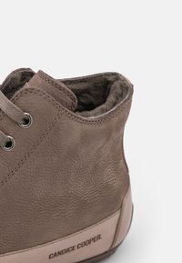 Bottine en cuir marron avec une finition texturée, fermeture à lacets et doublure en fourrure douce visible sur le bord supérieur. Logo de la marque sur le talon.