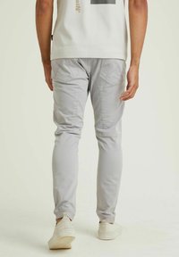 Lichtgrijze slim-fit broek met achterzakken en stikseldetails, gecombineerd met een licht shirt en witte instappers.