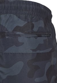 Dunkle Camouflage-Shorts aus strukturiertem Stoff mit elastischem Bund und einer hinteren Reißverschlusstasche für sichere Aufbewahrung.