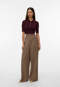 Polo de punto burdeos con cuello y detalle de botones, combinado con pantalones anchos de cintura alta de color marrón. Textura suave y corte ajustado.