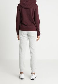 Felpa cappuccio bordeaux con finitura testurizzata, abbinata a pantaloni jogger grigi chiari, caratterizzati da gambe affusolate e polsini elasticizzati, completata da sneakers bianche.