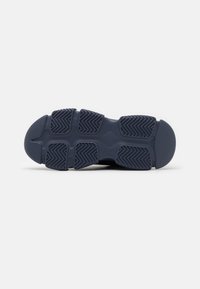 Shoe sole in dark navy rubber featuring a textured pattern with diagonal grooves and circular accents for grip and traction.