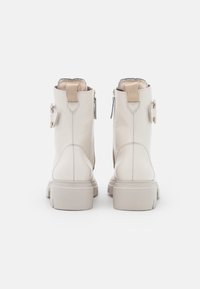 Béžové kotníkové kožené boty s texturovaným povrchem, vybavené bočním zipem, ozdobným páskem a robustní gumovou podrážkou.