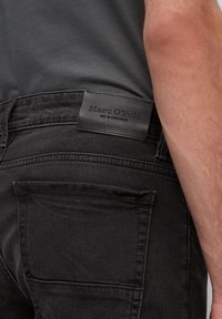 Jeans negros con un acabado texturizado, que presentan un parche de marca de cuero en la cintura y un gran bolsillo trasero.