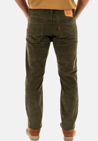 Pantalones de pana verde olivo con una textura suave, detalles de bolsillo trasero y una etiqueta de cuero marrón en la cintura.