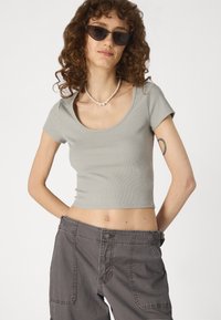 Szürke, bordázott, rövid ujjú crop top, mély dekoltárral, sötétszürke nadrággal párosítva, amely több zsebbel és gombos záródással rendelkezik.
