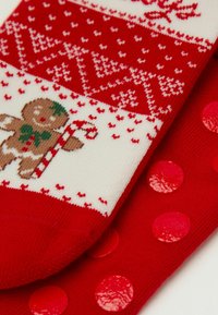 Červené a bílé pletené ponožky s designem perníkového mužíka a cukrové hole, s texturovanými červenými puntíky na podrážce. Jemná tkanina.