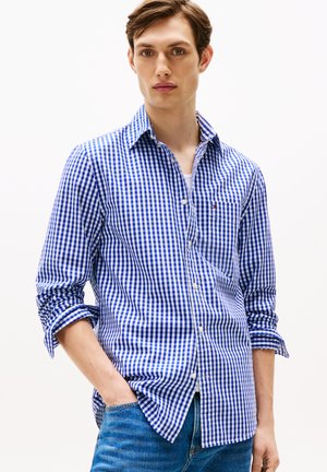 Camicia a quadri blu e bianchi con colletto button-down, maniche lunghe arrotolate e taschino sul lato sinistro del petto. Tessuto di cotone.