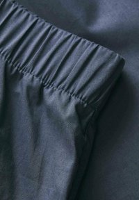 Tela de color gris oscuro con una cinturilla elástica fruncida. Textura suave y un ligero brillo, que destacan las cualidades ligeras y flexibles de la tela.