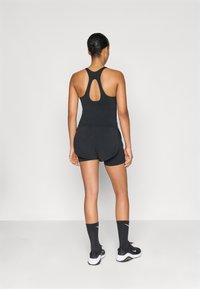 Melns sporta tanka ar atslēgas caurumu aizmugurē, pārī ar melnām šortiem. Modelis valkā melnas zeķes un apavus, uzsverot sporta apģērbu.