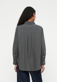Camicia grigia a righe con maniche lunghe, polsini con bottoni, yoke posteriore e vestibilità rilassata. Realizzata in un tessuto morbido con una leggera trama.