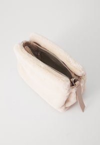 Faux fur veske i kremfarge med myk tekstur, rektangulær form, glidelås-lukking og lærstroppesmykke. Interiør vist.