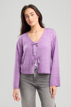 Purple cropped cardigan with a V-neck, drawstring front, long sleeves, and soft texture, paired with grey high-waisted jeans.