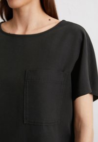 Schwarzes kurzärmeliges Oberteil aus Baumwolle mit weitem Ausschnitt und einer Brusttasche. Geschmeidige Textur und lässige Passform.
