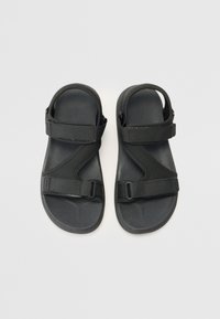 Svarta sandaler med justerbara remmar, tillverkade av syntetiskt material. Har en texturerad sula för grepp och en enkel design.