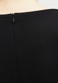 Czarna tkanina o fakturze z niskim dekoltem, z małym suwakiem z tyłu. Prosty i minimalistyczny design.