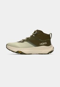 HOKA pārgājienu apavi ar vieglu, pelēki zaļu augšdaļu, elpojošu sietu, mīkstu apkārtni un Vibram zoli uzlabotai saķerei.