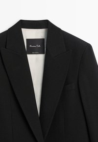 Czarna marynarka o strukturalnym kroju, z klapami w szpic, pojedynczą kieszenią na piersi i jasną podszewką. Metka z napisem "Massimo Dutti, Made in Portugal".