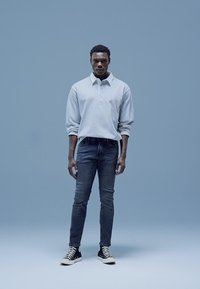 Šviesiai pilka, ilgomis rankovėmis polo marškinėliai, tamsios aptemtos džinsai, juodi aukštakulniai sportbačiai. Paprastas, šiuolaikiškas dizainas su laisvu prigludimu.