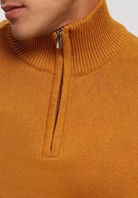 Jasnopomarańczowy sweter z wysokim kołnierzem i ćwierć zamkiem. Posiada prążkowany teksturę wokół szyi oraz miękki materiał.