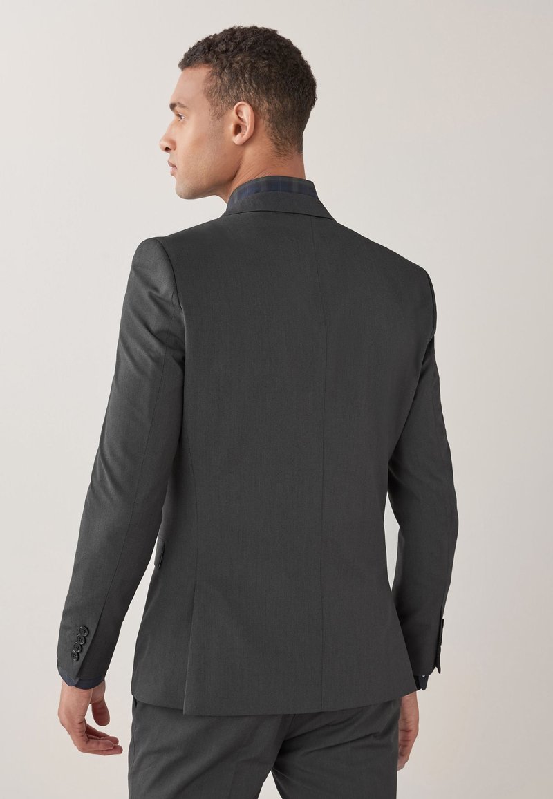 Giacca su misura grigio scuro, caratterizzata da una texture liscia, un design strutturato e dettagli di cucitura discreti sulle maniche e sulla schiena.