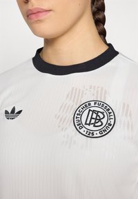 White jersey with black collar, featuring ribbed texture; Adidas logo and circular embroidered Deutscher Fußball-Bund badge.