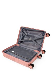 Hartschalenkoffer in sanftem Pink, mit einem geräumigen Innenraum mit grauem Futter, Quergurten und einem mit Reißverschluss versehenen Netzfach. Vier schwarze Rollen.