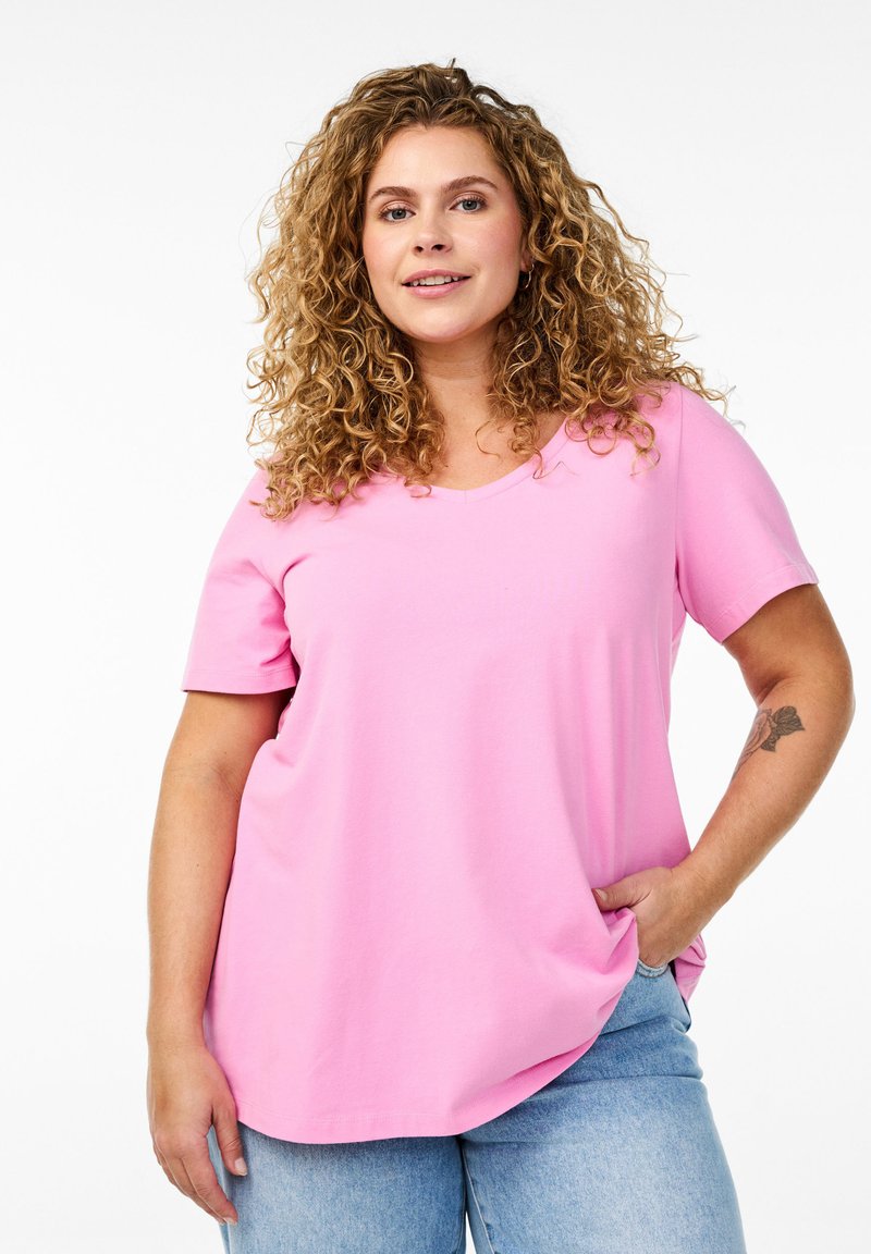 Camiseta de algodón rosa con escote en V y mangas cortas, con un corte holgado y textura suave. Combinada con jeans de mezclilla azul claro.