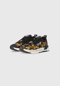 Baskets noires avec un motif baroque doré audacieux. Elles ont une surface texturée, des lacets noirs et un marquage Versace Jeans Couture.