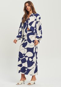 Completo bicolore blu navy e bianco con una camicia a maniche lunghe e bottoni morbida e una gonna a vita alta, realizzato in tessuto leggero.
