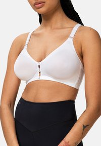 Biały bezprzewodowy biustonosz o gładkiej fakturze, z szerokimi regulowanymi ramiączkami i zapięciem z przodu z dwoma ozdobnymi haczykami. Czarne, wysokie szorty.