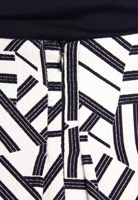 Woven fabric featuring a white background with bold black linear patterns; includes a vertical zipper detail at the center.