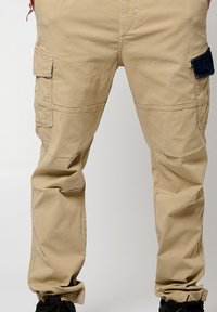 Beige cargobroeken met meerdere zakken, elastische boorden en een klittenbandsluiting. Gemaakt van duurzaam materiaal met een soepele textuur.