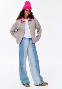 Světle šedá bomber bunda s růžovým límcem, bílý tričko, oversized světle modré džíny a boty s leopardím potiskem, na hlavě růžová pletená čepice.