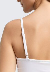 Weißes enganliegendes Trägershirt mit dünnen verstellbaren Trägern und einer geschlungenen Detailführung auf der Rückseite, gefertigt aus einem glatten, leichten Stoff.