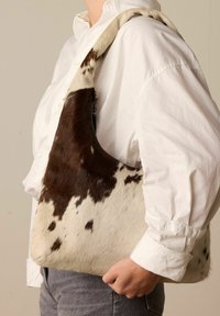 Golfdijen tas met een bruin-wit gevlekt patroon, gebogen vorm en zachte textuur; over de schouder gedragen met een ritsluiting.