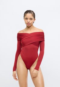 Punane pika varrukaga ühes tükis ujumistrikoo õlavaba kaelusega, kogutud kangade detailide, kõrgete külgedega ja siledaga tekstuuriga.